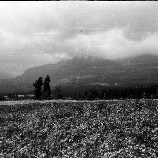 Rural landscape with snow-covered field, distant mountains, and stormy sky.