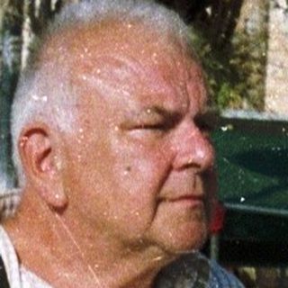 Man walking outdoors in casual attire near palm trees.