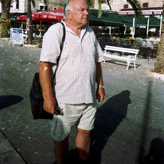 Man walking outdoors in casual attire near palm trees.