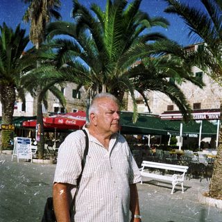Man walking outdoors in casual attire near palm trees.