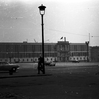 Large building with vintage car and lone pedestrian.