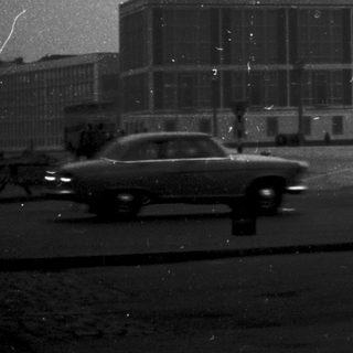 Large building with vintage car and lone pedestrian.