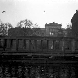 Classic building by waterfront, overcast sky, leafless trees.