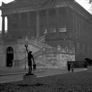 Neoclassical building with grand staircase, statues, and people.