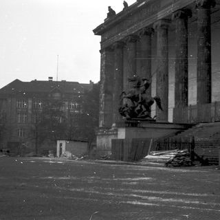 Damaged neoclassical building with equestrian statue post-war.