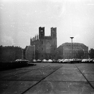 Historic cathedral with vintage cars in parking area.