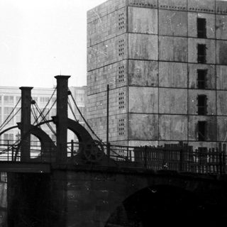 Vintage bridge over water with industrial buildings.