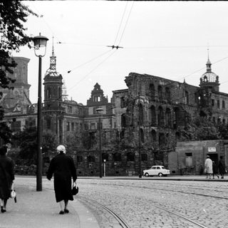 War-damaged city buildings with pedestrians walking.