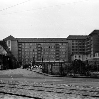 Urban street with mid-century apartment buildings and barbed wire fence.