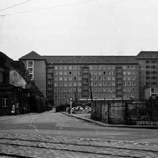 Urban street with mid-century apartment buildings and barbed wire fence.