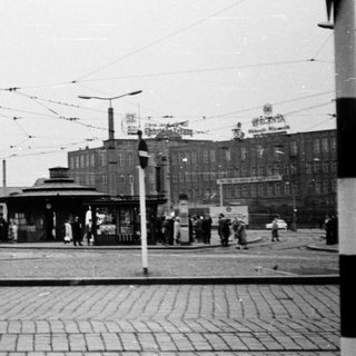 Busy urban tram stop with pedestrians and vintage vehicles.