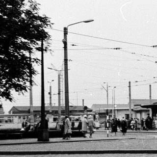 Busy urban tram stop with pedestrians and vintage vehicles.