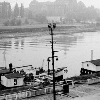Steam-powered barge on river near historic buildings.