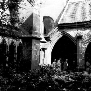 Damaged historic building with rubble and people inspecting ruins.