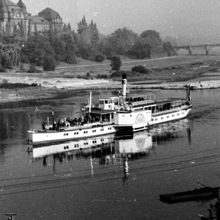 Historic building by river with vintage boat.