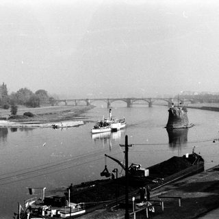 Historic river scene with bridge, boats, and industrial docks.