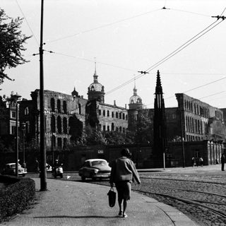 Mid-20th century urban street scene with tram tracks, vintage cars, and historic architecture.