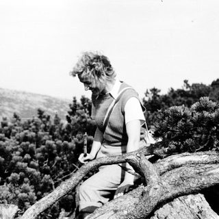Person carving wood while seated on rocky outcrop.