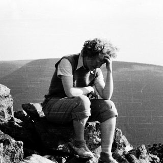 Person sitting on rocks, contemplating mountain landscape.