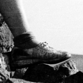 Person sitting on rocks overlooking open landscape.