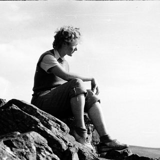Person sitting on rocks overlooking open landscape.