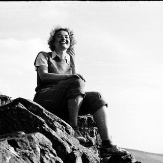 Woman smiling while sitting on rocky cliffside.