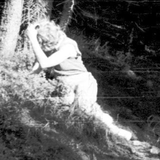 Silhouette of person sitting alone in dark forest.