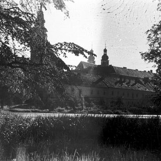 Historic building with church tower behind trees.