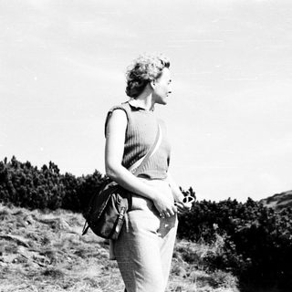 Woman standing outdoors on hillside, holding bouquet.