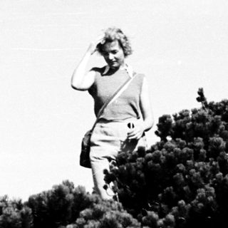 Person standing on hilltop, shielding eyes.