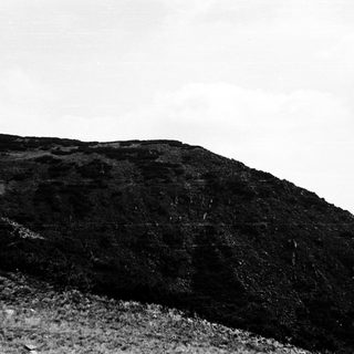 Cliffside with lone climber ascending rocky slope.