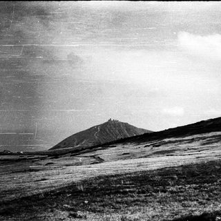 Mysterious hilltop structure in stormy landscape.