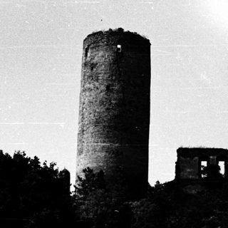 Towering stone watchtower ruins in forested hillside.