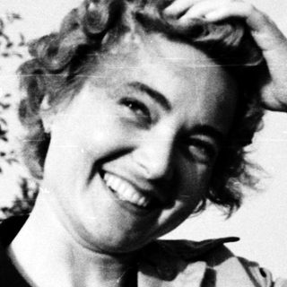 Smiling woman outdoors, hand on shoulder, mid-20th century.
