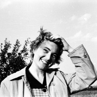 Smiling woman outdoors, hand on shoulder, mid-20th century.