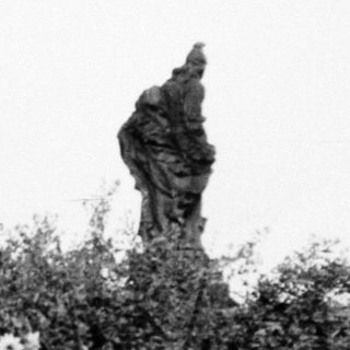 Statues in overgrown garden with blooming shrubs.