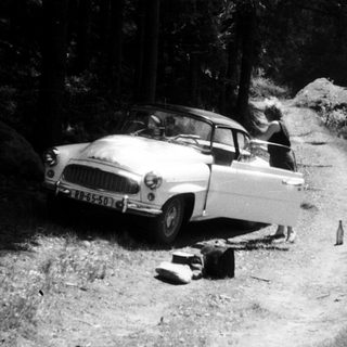 Classic car parked on uneven forest road.