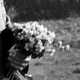 Man in vintage suit holding wreath outdoors.