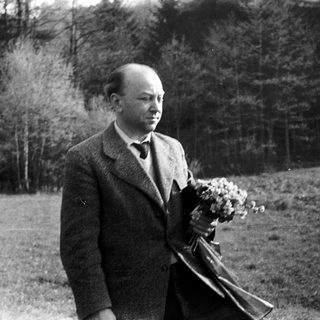 Man in vintage suit holding wreath outdoors.