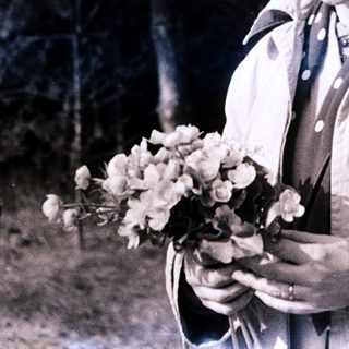Woman holding flowers outdoors in vintage-style photo.