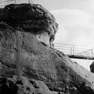 Steep rock cliff with suspension bridge above.