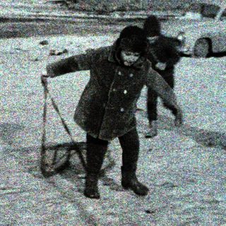 Children sledding in snowy urban street with adult supervision.