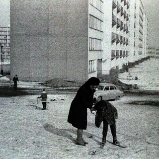 Snowy urban street with woman helping child cross.