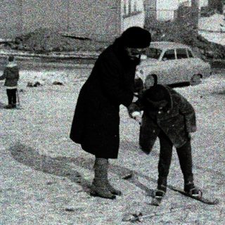 Snowy urban street with woman helping child cross.