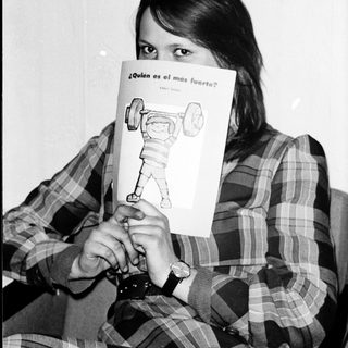 Person holds book with question "¿Quién es el más fuerte?" featuring strongman illustration.