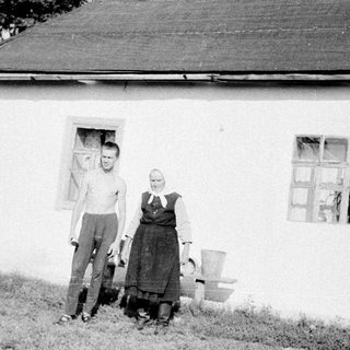 Two people posing outside a rural house.