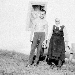Two people posing outside a rural house.