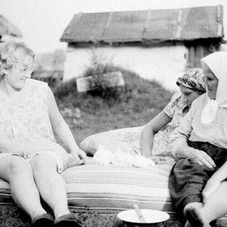 Two women and a child resting outdoors near a barn.