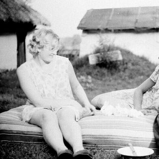 Two women and a child resting outdoors near a barn.