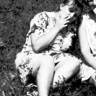 Two people sitting closely outdoors in grassy field.
